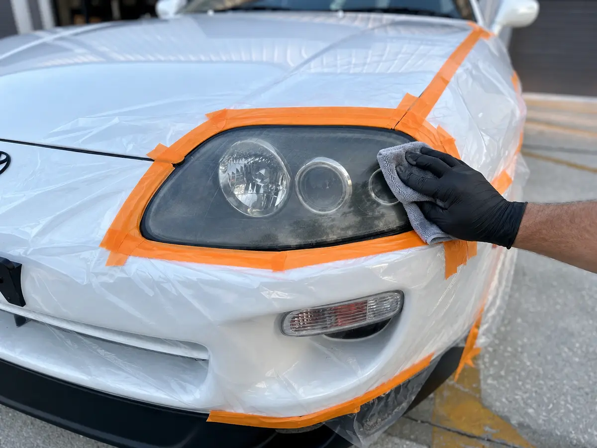 White Toyota Supra headlight protected with masking film while the oxidized lens is cleaned